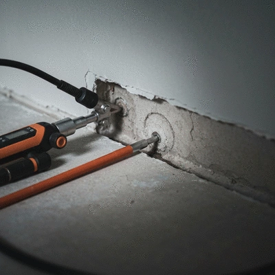Plombier utilisant un équipement de détection de fuite pour localiser une fuite dans un mur, avec des outils modernes, mettant en évidence la détection non-destructive